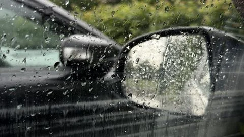 Raindrops on a black vehicle's side mirror and window. Close-up view of a wet Stock Photos