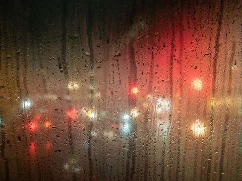 Raindrops on a bus window with blurred headlights behind Stock Photos