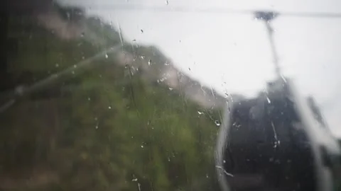 Raindrops on a cable car window capturing a passing gondola and misty mountain Stock Footage 345338350