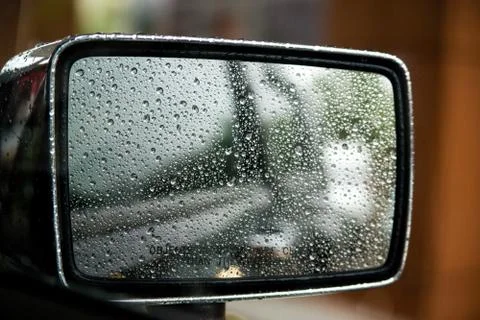 Raindrops on car mirror with side wing mirror. Rainy day on the road Stock Photos