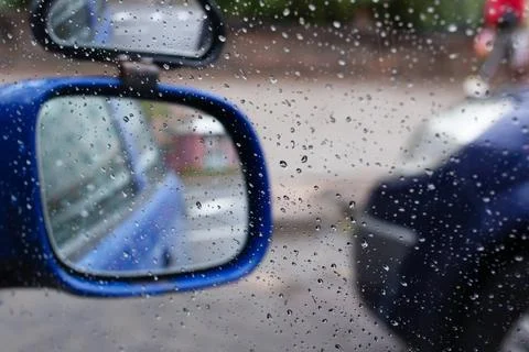 Raindrops on car side view mirror and window closeup. Bad weather driving Stock Photos