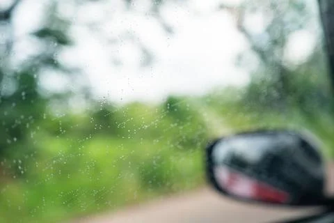 Raindrops on car window with side rear view mirror blurred in background. Stock Photos