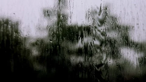 Raindrops cascade down a window, creating a blurred view of the outside world. A Stock Footage 313500695