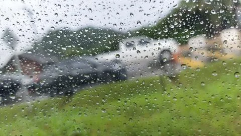 Raindrops cascade down a window pane, softly blurring the view of cars and .. Stock Photos