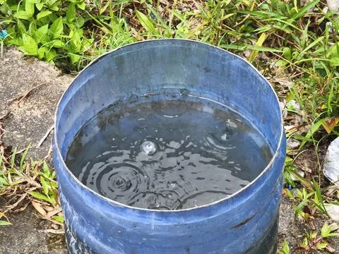 Raindrops Causing Ripples on Water Surface in a Blue Barrel Foto stock
