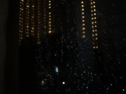 Raindrops cling to a windowpane offering a blurry view of distant city lights Fotos Stock