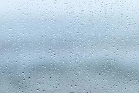 Raindrops cluster on a window pane during a grey overcast day, creating a s.. Stock Photos