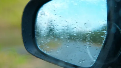 Raindrops covering car side mirror reflecting road during rainy day Stock Footage 323279582