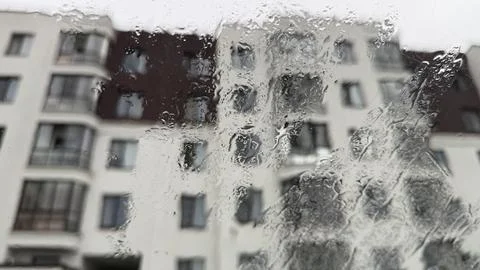 Raindrops covering a glass surface with a blurred view of a modern multi-story Stock Photos
