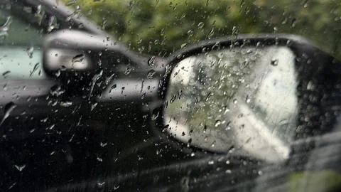 Raindrops covering a window pane. Blurred background reveals green trees and a Stock Photos