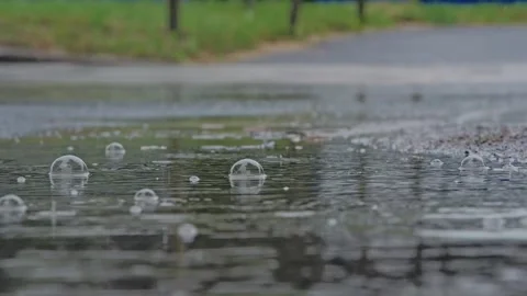 Raindrops Create Puddle Bubbles, Moving Cars Reflected Across Rainy Urban Road 库存影片 348766942