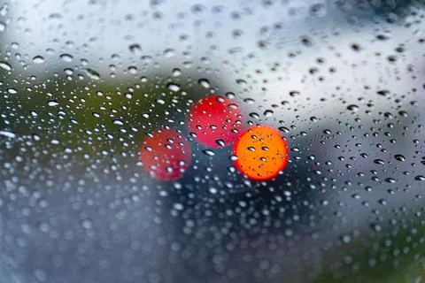 Raindrops create a textured effect on the car window, blurring bright red l.. Stock Photos