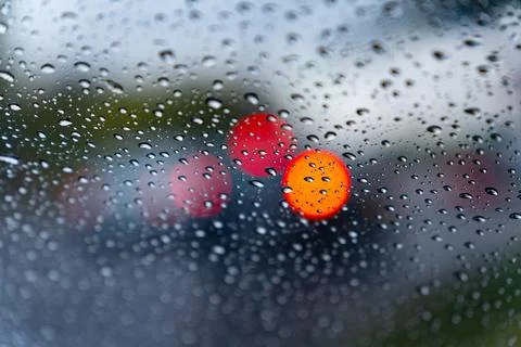 Raindrops create a textured pattern on a car window, blurring red and orang.. Stock Photos