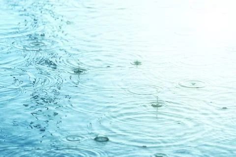 Raindrops creating concentric circles and droplets on water surface Foto stock