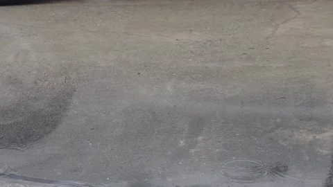 Raindrops creating ripples on the water surface. Dark grey concrete road te.. Video stock 338394618