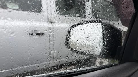 Raindrops dotting a car window, partially obscuring the blurred shape of a Stock Photos