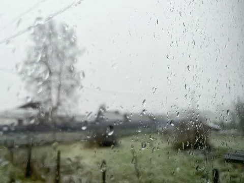 Raindrops down a windowpane, creating a blurred view of the outdoor landscape Stock Photos