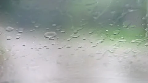 Raindrops fall and flow down a windowpane, wipers intermittently cut throug.. Stock Footage 255767432
