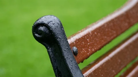 Raindrops fall on a cast iron and wooden park bench in the spring Stock Footage 95206348