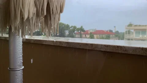 Raindrops fall on the parapet and folded parasol on the balcony. Stockbeeldmateriaal 164526596
