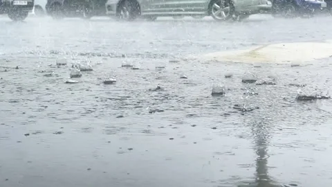 Raindrops fall into a puddle on a city street against the backdrop of cars  Stock-Footage 244241195