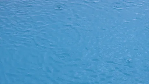 Raindrops fall on surface of pool, forming circles and bubbles. Abstract Stock Footage 141527402
