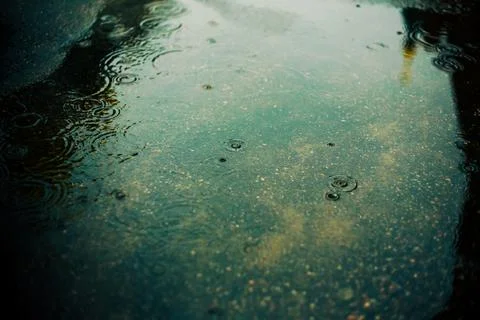 Raindrops fall on the water surface of a puddle on the street in the city and Stock Photos