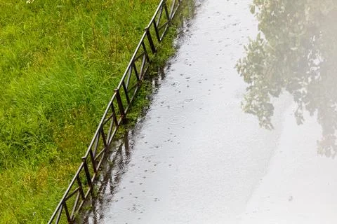 Raindrops fall on a wet path beside green grass Stock Photos