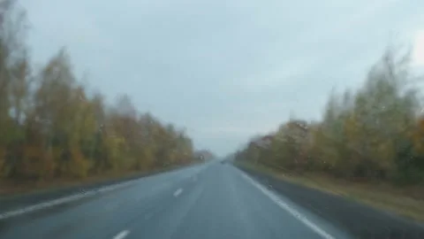 Raindrops fall on the windshield while driving on the autumn highway Video stock 142206934
