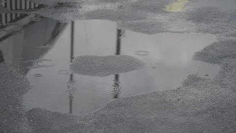 Raindrops falling into asphalt puddle reflecting overcast sky and railing. Stock Footage 331719423