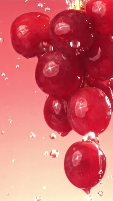 Raindrops falling on a branch of red grapes on a pink background. Filmed on a Stock Footage 335313890