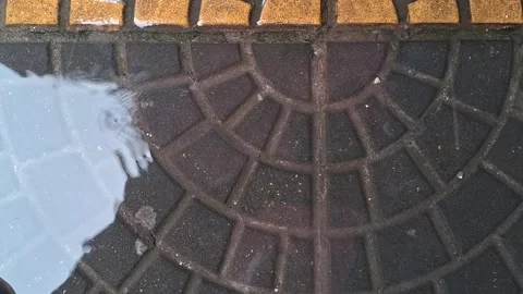 Raindrops falling into puddle on patterned pavement Stock Footage 345009974