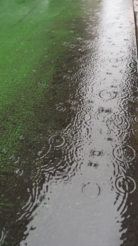 Raindrops falling into a puddle on wet asphalt vertical video Stock Footage 346848945