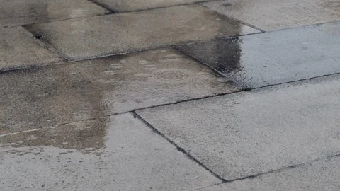 Raindrops falling in slow motion on pavement in city. Low angle, close up. 動画素材 116387072