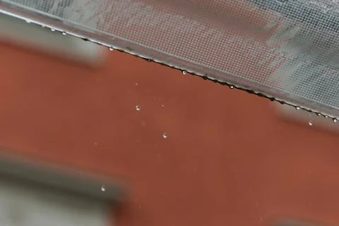 Raindrops falling from transparent canopy with red house in blurred backgroun Stock Photos