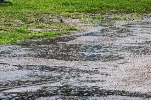 Raindrops falling on a wet asphalt surface with green grass nearby Foto stock