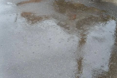 Raindrops falling on a wet asphalt surface creating ripples and reflections Stock Photos