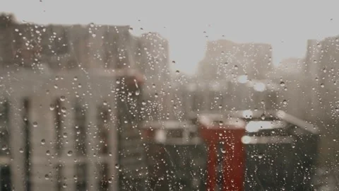 Raindrops falling on a window glass with a blurry urban city background Stock Footage 346520716
