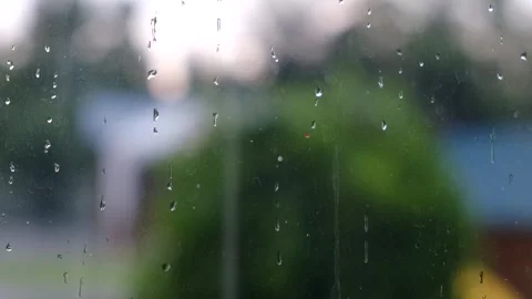 Raindrops flowing down window glass pane with blurry green foliage background Video stock 338198431