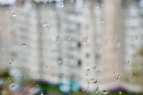 Raindrops on the glass close-up. Behind them is a blurry background of houses. Stock Photos