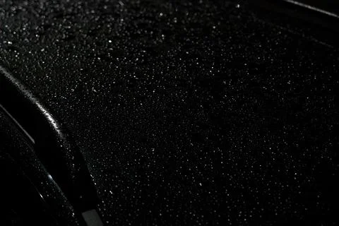 Raindrops glisten on a dark surface at night after an evening shower Stock Photos