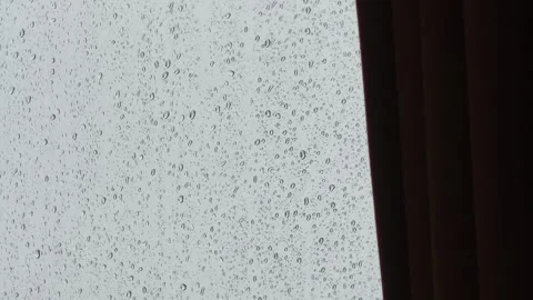 Raindrops hit the windowpane with the curtain in the foreground, a rainy day. Stock Footage 340557434