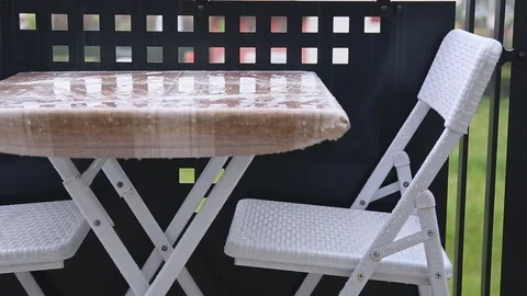 Raindrops hitting empty simple table and chairs standing near a balcony railing Stock Footage 129388189