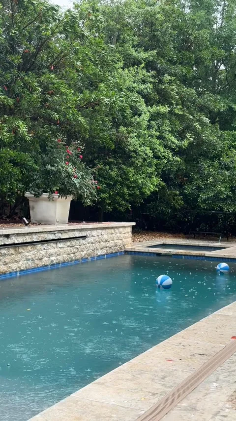 Raindrops ripple serenity in backyard pool as floating ball drifts gently Stock Footage 315524689