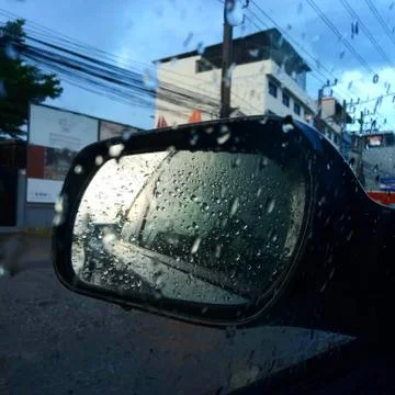Raindrops on side rear-view mirror an a car in a raining day Stock Photos