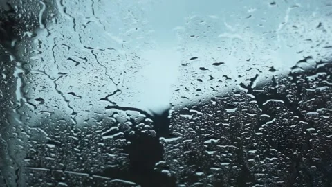 Raindrops sliding down a windowpane with a blurry view of a house Stock Footage 334845234
