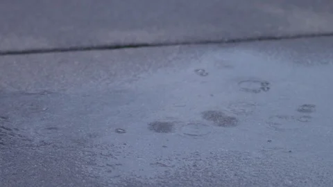 Raindrops splashing into puddle on concrete road in slow motion. Stock Footage 86568965