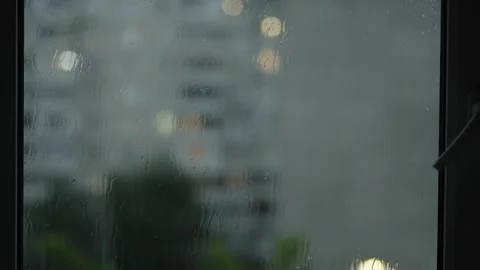 Raindrops streaming down window glass with blurred city lights background Stock Footage 336732165