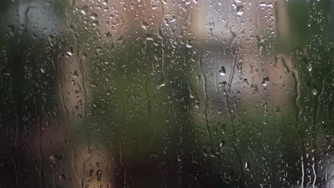 Raindrops streaming down a window pane with blurred natural background scenery Video stock 347065654