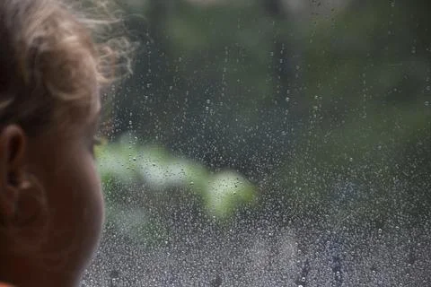 Raindrops on the surface of a window pane with a blurred silhouette of a girl Stock Photos